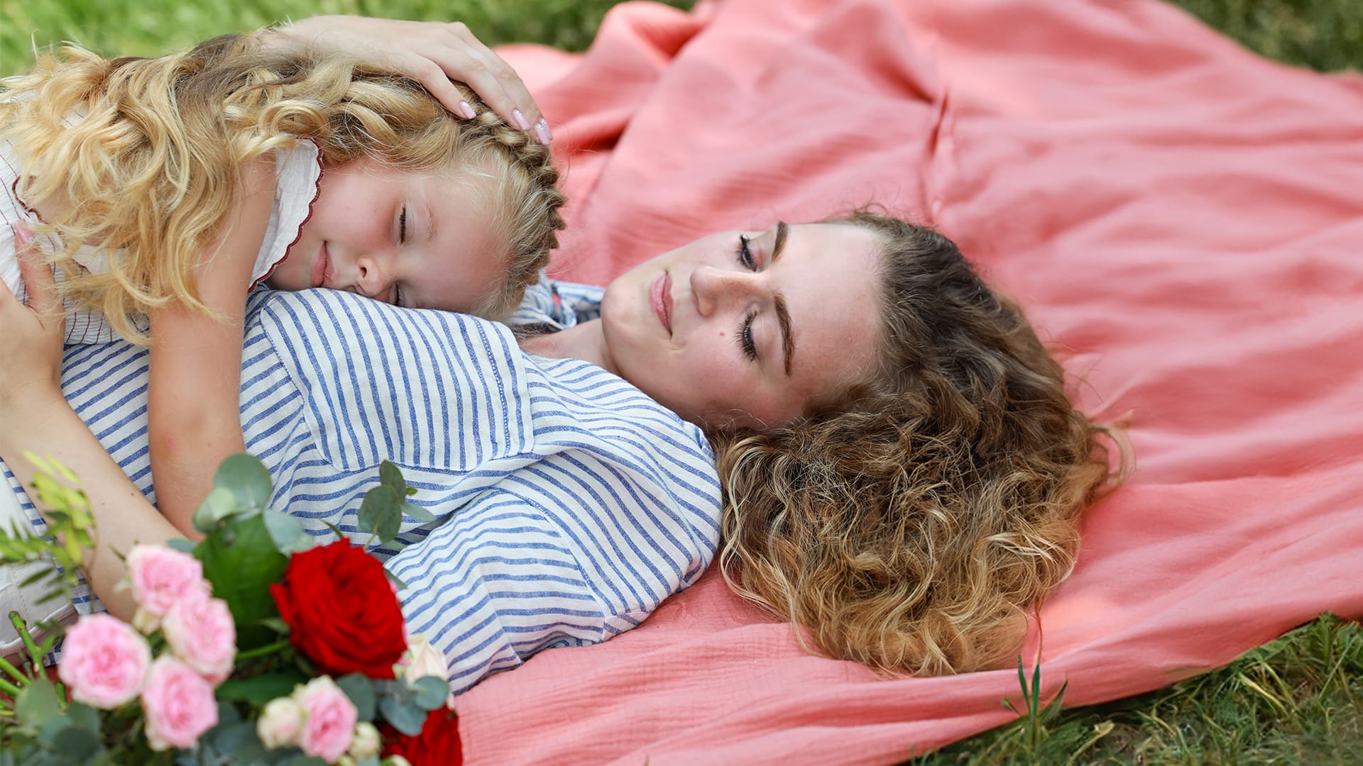 mor og datter med buket i hånden ligger på tæppe i naturen