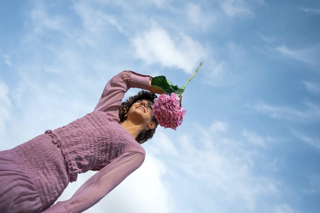 en ung kvinde på en mark med en stor lyserød blomst i hånden