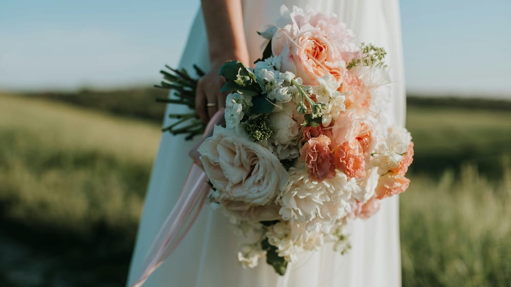 brud holder smuk buket i koral og lyse toner