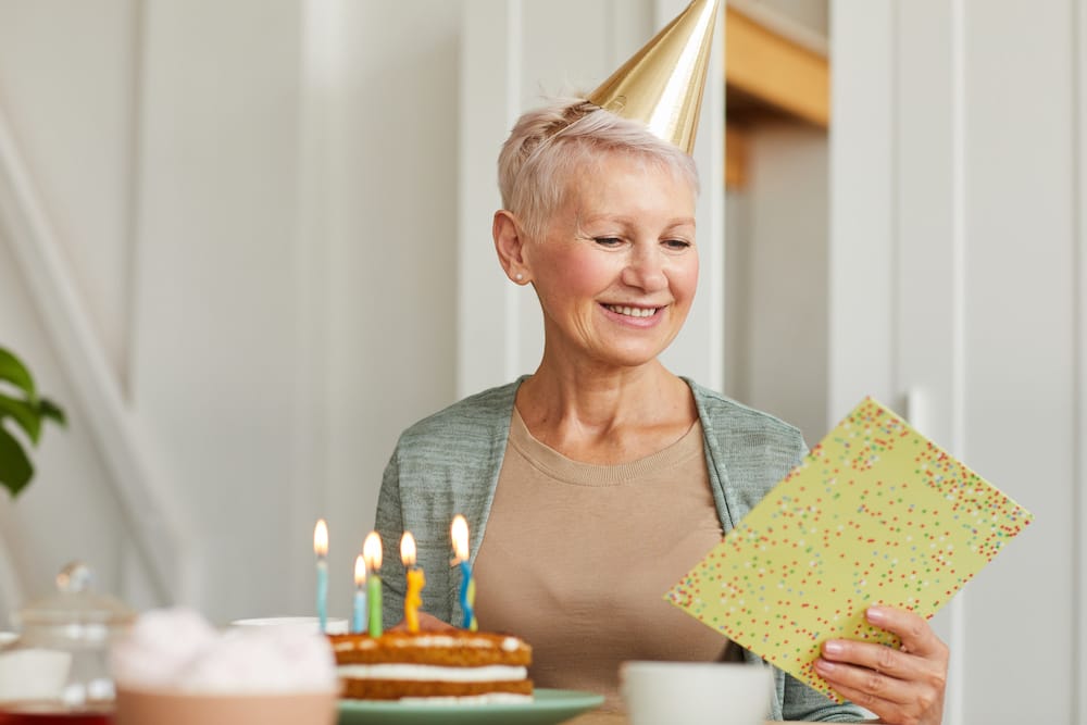 Kvinde med festhat læser glad fødselsdagskort med lagkage med lys på bordet