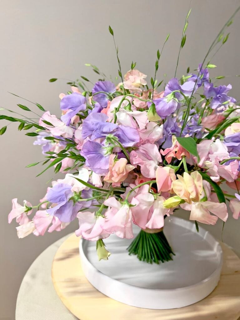 Unik buket i lilla og lyserøde nuancer af blomster stående i fad