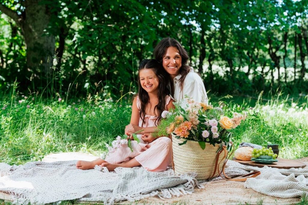 smilende mor og datter på skovtur med smukke blomster i stråtaske