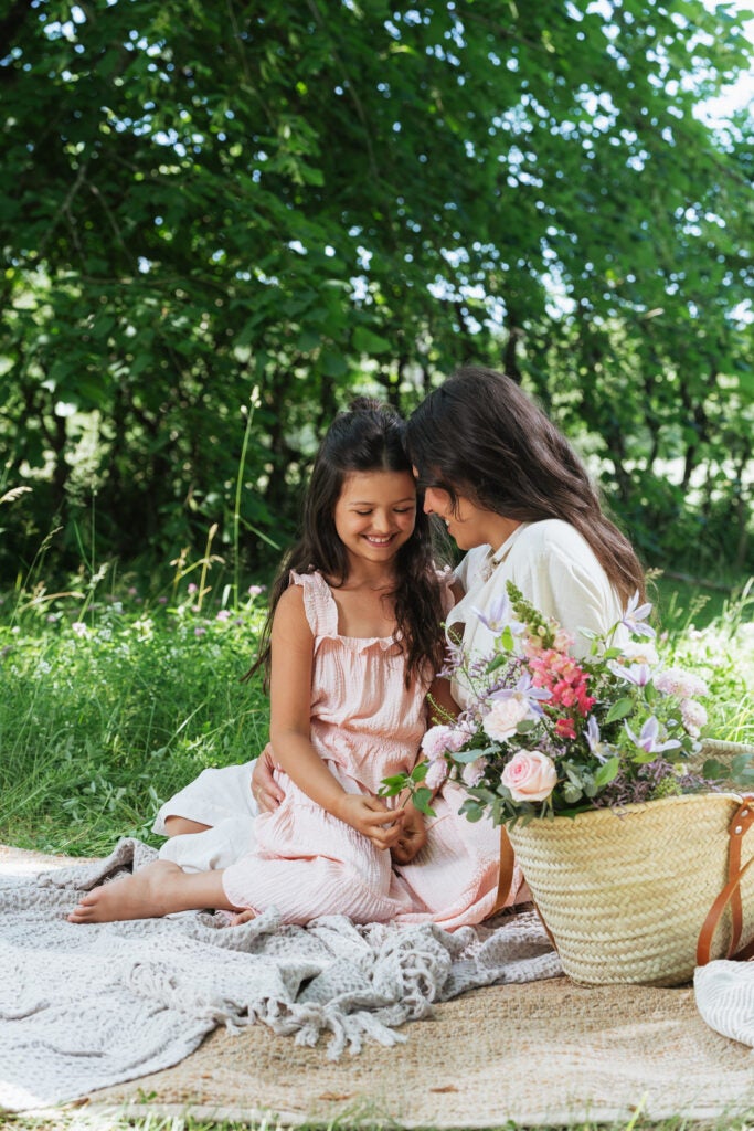 mor og datter på picnictæppe med blomsterkurv