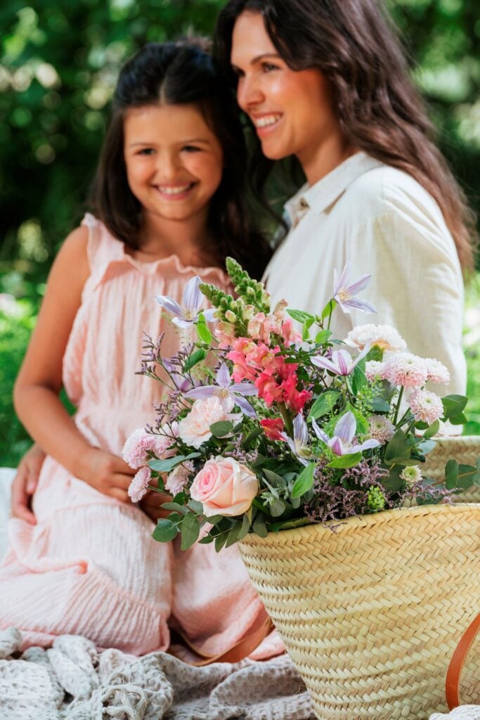 Mor og datter på picnictæppe med blomsterkurv