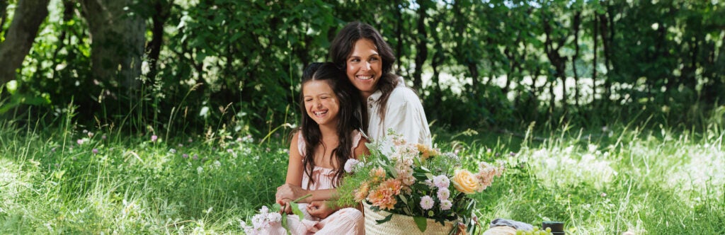 Mor og datter på picnictæppe med blomsterkurv