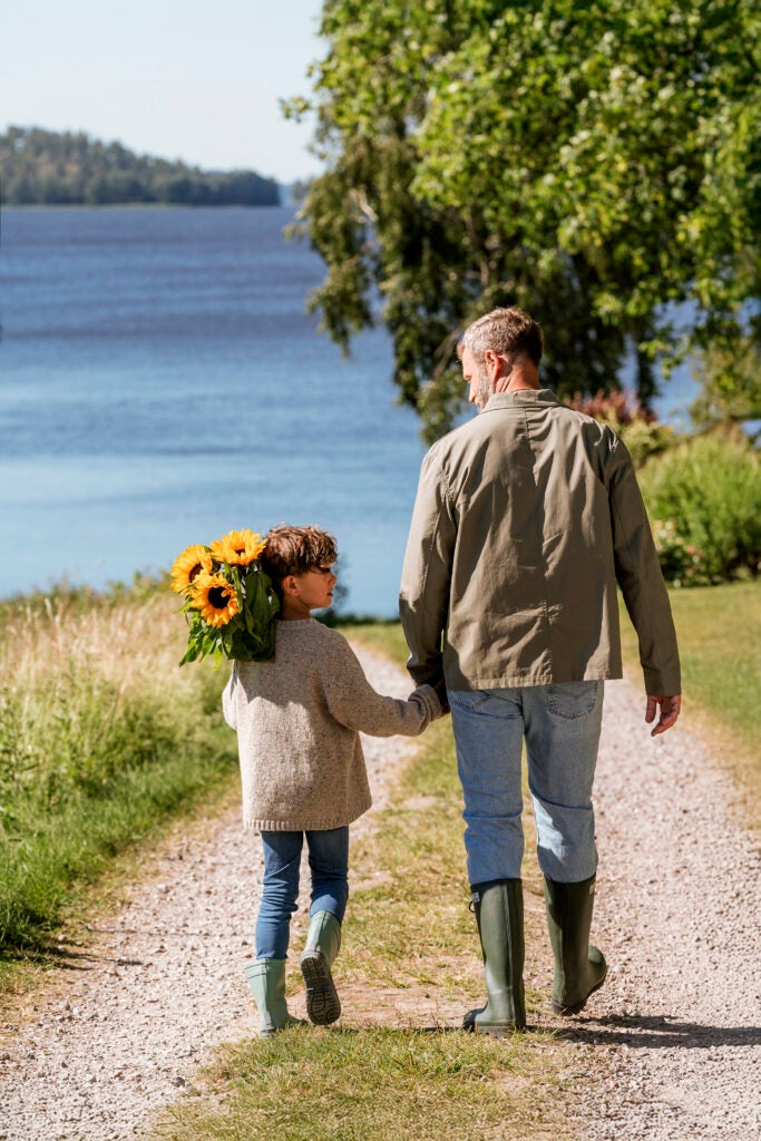far og søn går mod vandet med en solsikkebuket