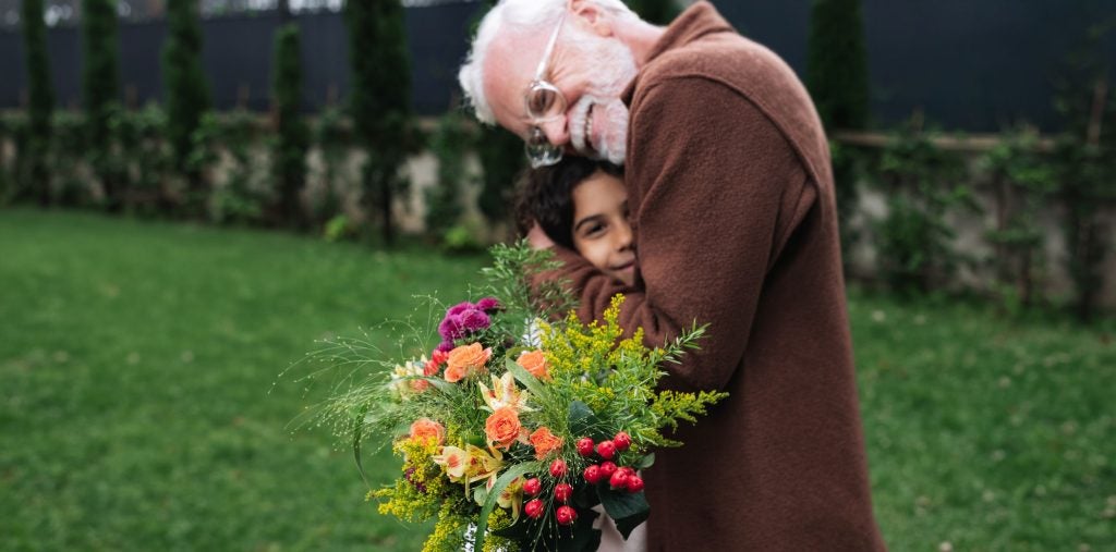 glad bedstefar og barnebarn står med blomsterbuket og krammer