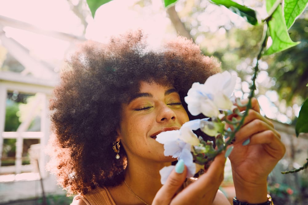 kvinde dufter smilende til blomst med lukkede øjne