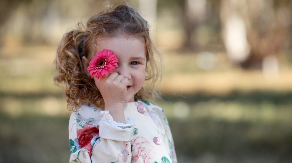 Pige i naturen holder pink blomst foran ansigtet
