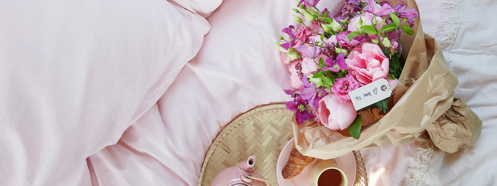 Fin lyserød Mors Dag-buket på seng