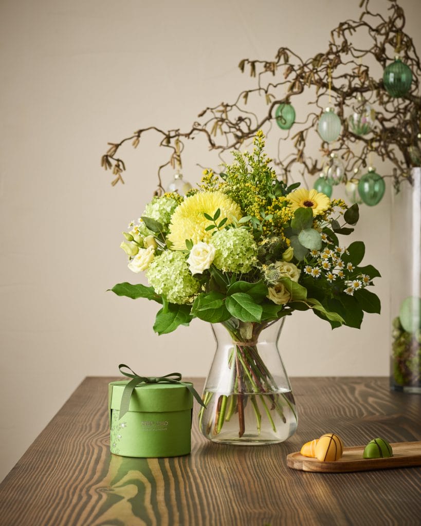 frodig grøn og gul påskebuket på bord med gave og påskeæg