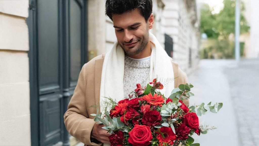 En mørkhåret mand på gaden med en buket røde blomster, bl.a. roser, nelliker og gerbera, i anledning af Valentinsdag.