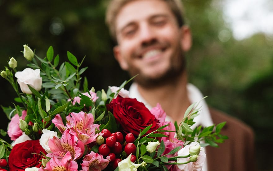 smilende mand modtager buket med lyserøde og røde blomster