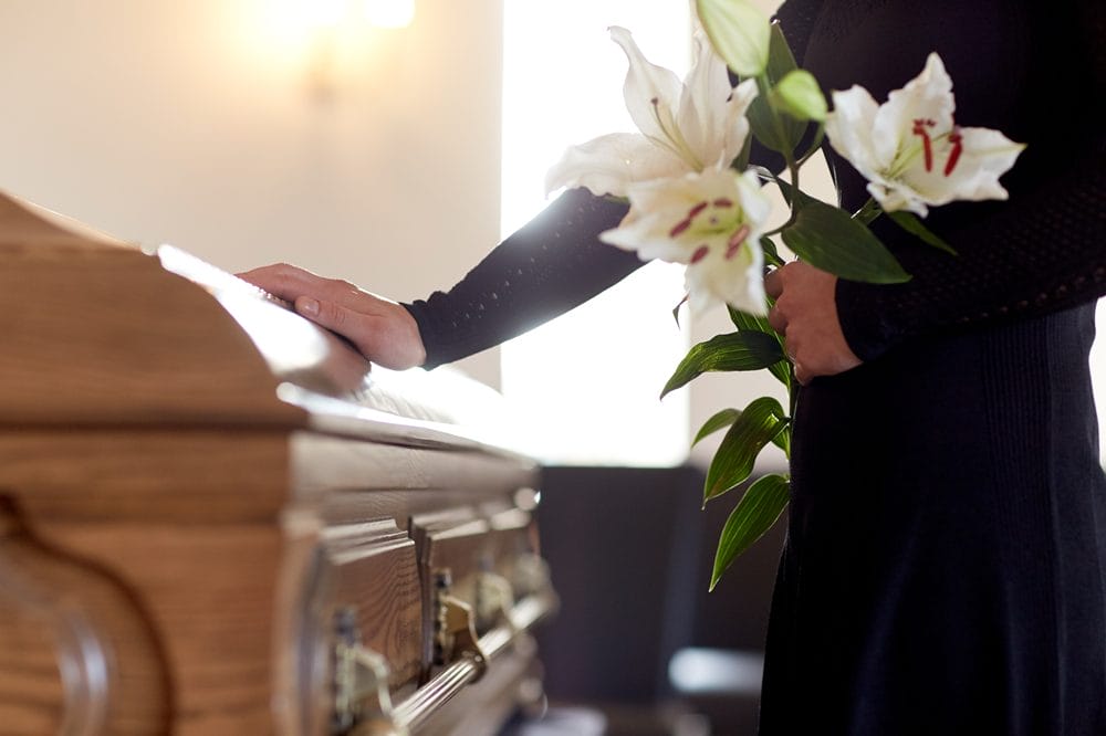 Person holder hånd på kiste med hvide blomster i armen