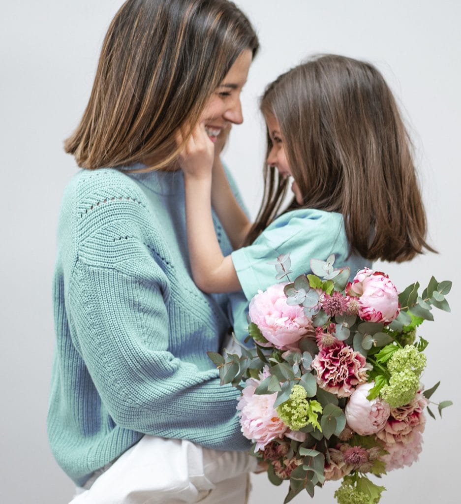 une mère tient sa fille dans ses bras ainsi qu'un bouquet de fleurs