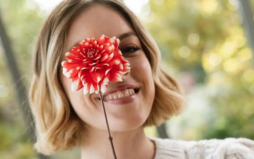 en kvinde smiler, mens hun holder en blomst foran sig