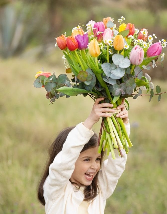 glad pige holder farverig tulipanbuket over hovedet